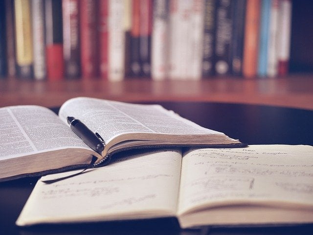Libros abiertos sobre una mesa con una estantería al fondo